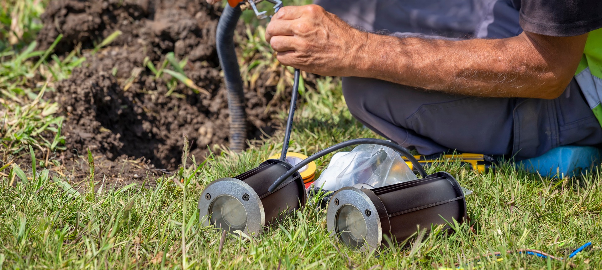 een installateur legt grondspots aan in een groen gazon